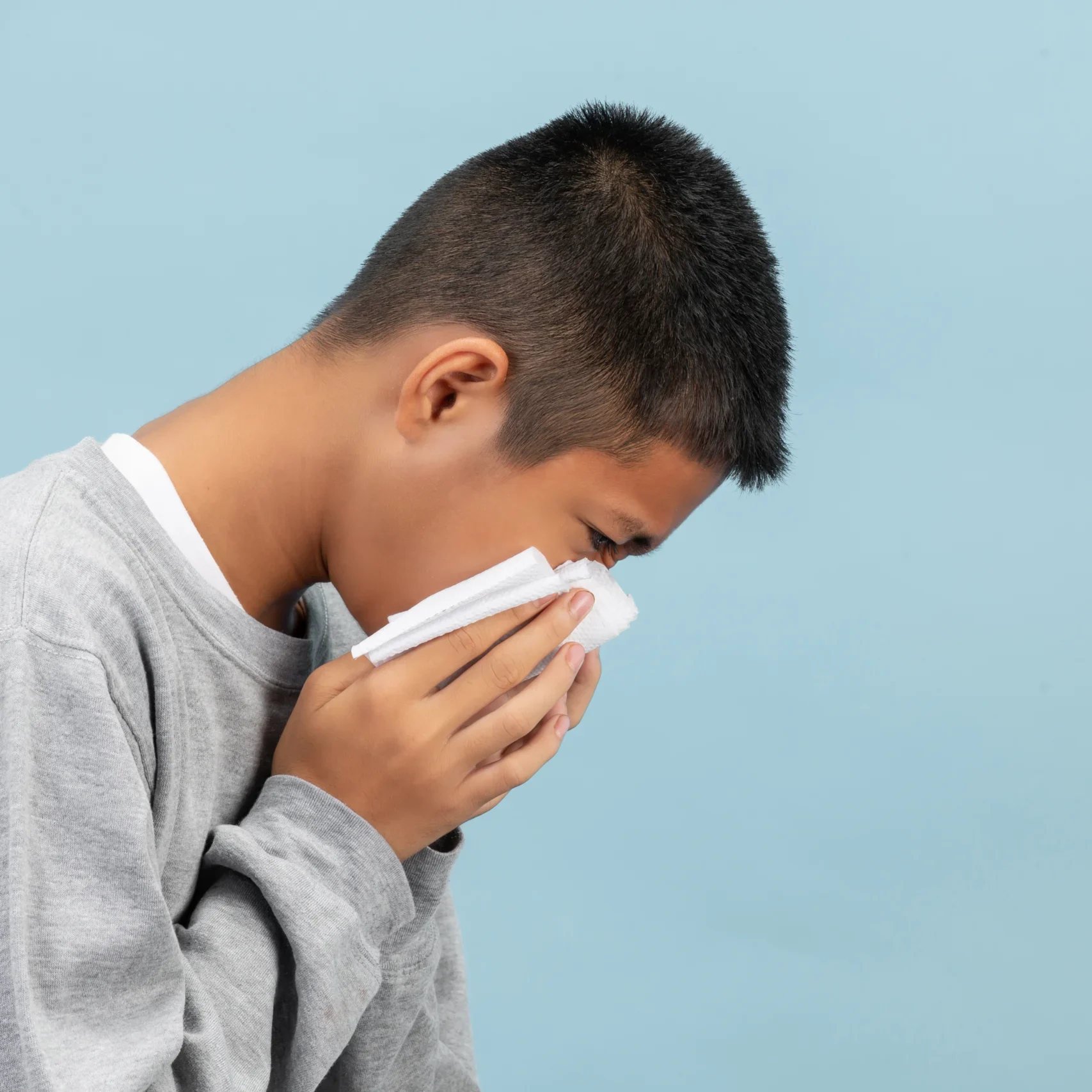 A boy is sneezing into tissue and feeling sick on blue backgroun